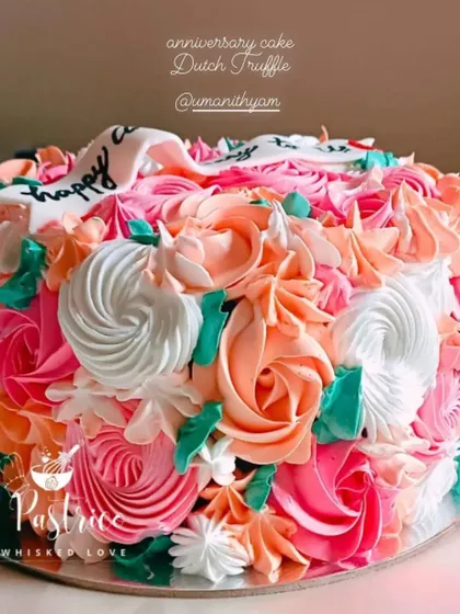 A Dutch truffle cake covered in a beautiful bouquet of piped flowers in shades of pink and peach for an anniversary.