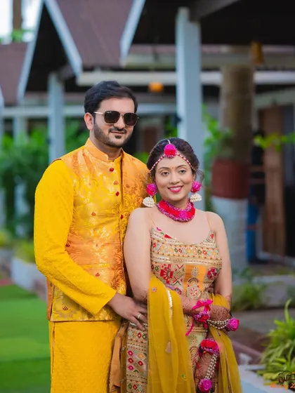 A classic couple portrait from a Haldi ceremony, with the groom in sunglasses and the bride in beautiful floral jewelry.