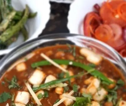 A top-down, slightly blurred view showing the vibrant red of the pickled onions against the deep brown of the chole. It captures the essence of a delicious, home-cooked Punjabi meal.