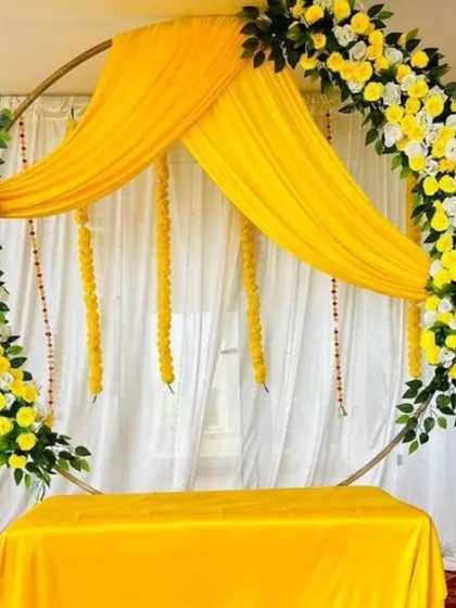 A simple and elegant backdrop for a Haldi or Mehandi ceremony. The circular frame is decorated with yellow and white flowers and draped with yellow fabric.