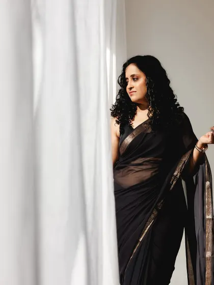 A pensive shot by the window. The natural light beautifully highlights her curly hair and the soft, subtle makeup.