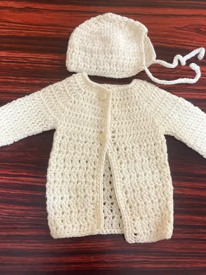 This classic off-white baby set includes a button-up cardigan and a matching bonnet, hand-stitched for a timeless and cozy feel.
