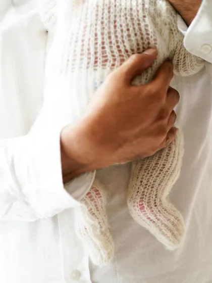 Sometimes, the smallest details tell the biggest story. This close-up of a father holding his newborn in a soft, knitted outfit highlights the delicate miracle of new life.