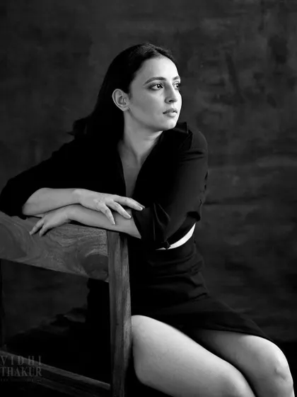 A pensive, cinematic portrait of an actor. The use of a simple wooden chair as a prop and the soft, directional light create a narrative quality, as if taken from a film still.