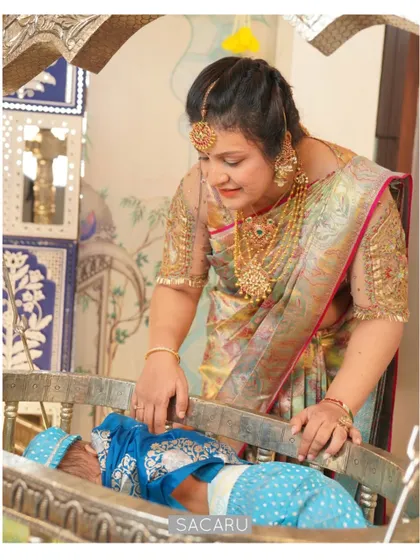 Our client Bhavna at her baby's naming ceremony, wearing a custom blouse with sheer sleeves and intricate cutwork embroidery.