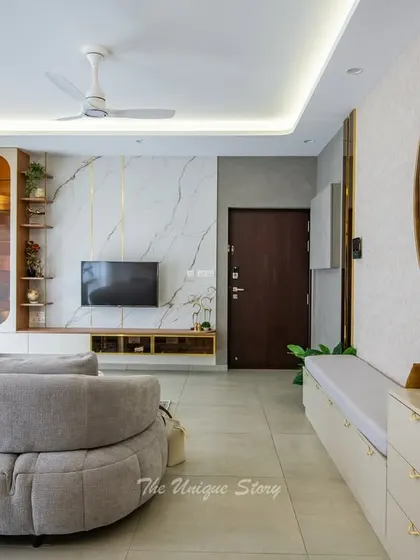 This living room features a unique curved sofa and a striking TV wall with a white marble finish and gold inlay. A custom bench with storage is accented by a large, circular piece of art, creating a functional and artistic focal point.