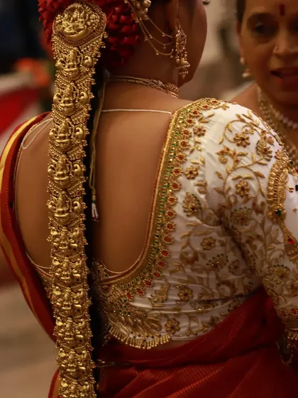 A view of the back of the heavily embroidered white blouse. The intricate floral zardosi work complements the bride and groom theme on the sleeves, creating a cohesive and stunning design.