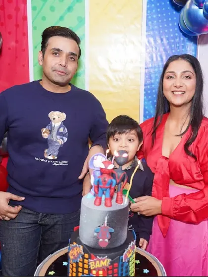 A happy family poses behind a Spider-Man themed cake, celebrating their son's birthday.