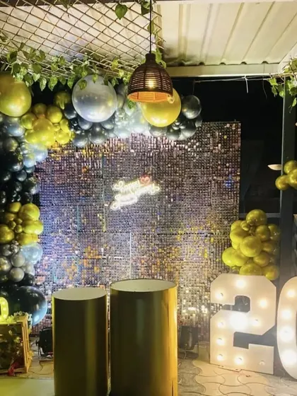 A rustic-glam birthday setup with a silver sequin wall and marquee numbers. The surrounding greenery and hanging lights add a unique touch to the decor.