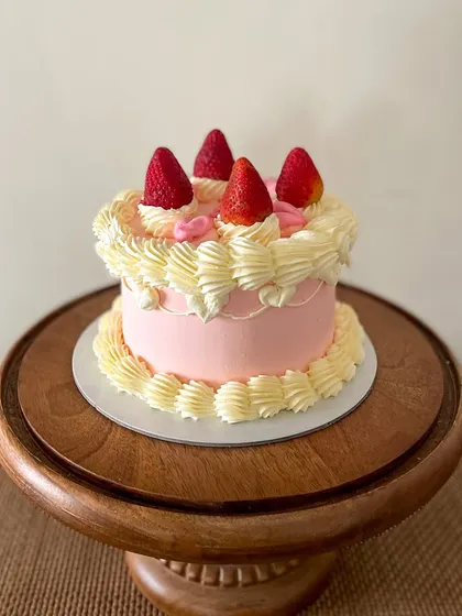 A sweet and simple vintage-style cake. This pink buttercream cake is decorated with classic piping, topped with fresh strawberries for a fresh and pretty look.
