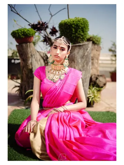 A regal portrait featuring stunning traditional jewelry and a vibrant pink saree. The outdoor setting adds a touch of natural beauty to this classic look.