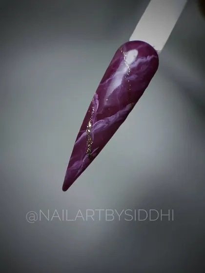 A single stiletto nail with a deep purple marble effect, accented with a fine line of gold glitter.