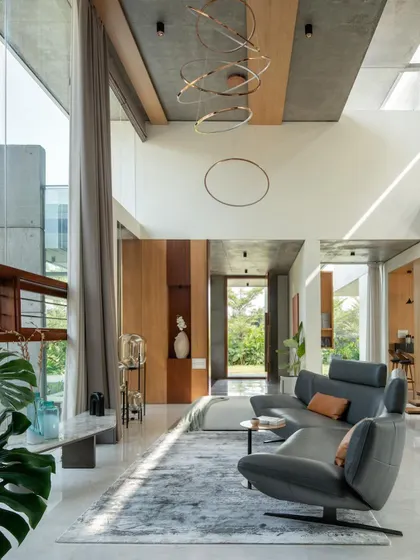 The double-height living room of The Quarry House, where sunlight streams in, highlighting the raw concrete ceiling and modern furnishings.