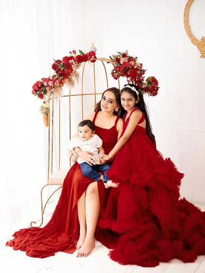 A mother and her two children in a gorgeous red-themed portrait. The older daughter's flowing gown matches her mother's, creating a striking visual.