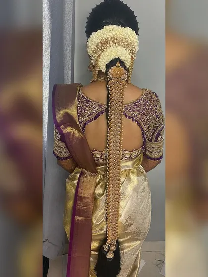 A full and grand Poola Jada, a traditional bridal hairstyle for a muhurtham. The entire length of the braid is covered in intricate golden ornaments and fresh flowers.