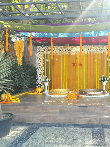 This Haldi setup on a raised wooden deck is perfect for a farmhouse or poolside event. We use a backdrop of marigold strings framed by white flowers, with two urlis ready for the ceremony.