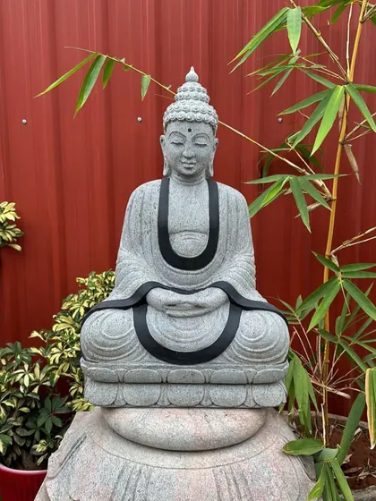 A beautifully detailed stone Buddha statue in a meditative pose, placed against a backdrop of bamboo.