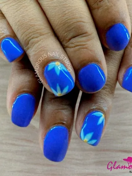 Bold blue nails are softened with the addition of hand-painted white and yellow floral accents, creating a beautiful contrast.