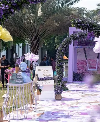 The entrance to a dreamy Haldi ceremony with a lilac and mint green color palette. Floral arches and a custom welcome sign greet the guests.