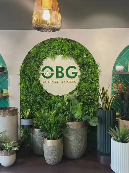 A detailed shot of our main branding wall, featuring an artificial green arch and our logo. This display showcases a variety of our planters, from rustic textured pots to sleek modern designs.