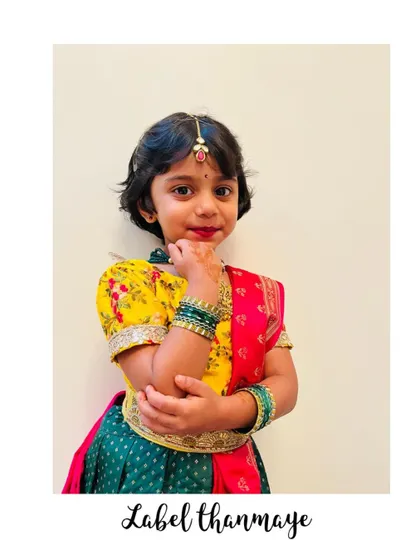 A colorful traditional lehenga set for a little girl. The dark green skirt is paired with a yellow embroidered blouse and a pink bandhani dupatta.