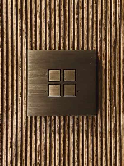 A detail of a brass switch plate set against a fluted wooden panel in the Worli Duplex. The combination of the machined metal and the natural wood grain is a recurring theme in our work.