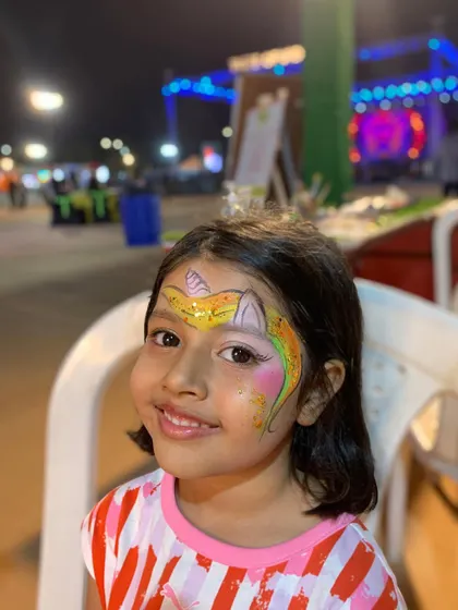 A happy client with her yellow and pink unicorn face paint, ready to enjoy the festival.