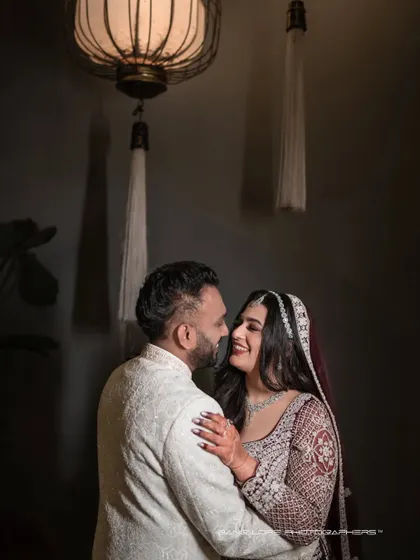 An intimate reception portrait, softly lit from above. The dark, moody background emphasizes the couple's bright smiles and the warmth of their interaction.