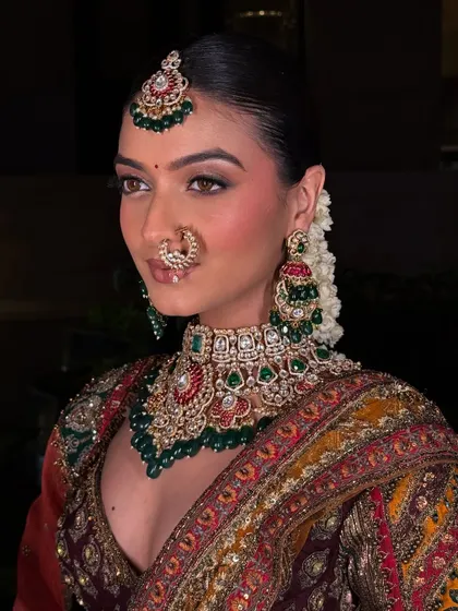 This is the kind of high-quality, professional look you can create with our rental collection. This model is wearing a complete bridal set, including a detailed choker with green and red accents, matching earrings, maang tikka, and nath.