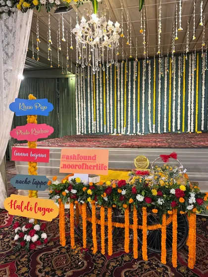 A fun and interactive decor piece for a Haldi event. A decorated cart holds colorful signs with hashtags and festive instructions like 'Haldi Lagao' and 'Nacho Tappo'.