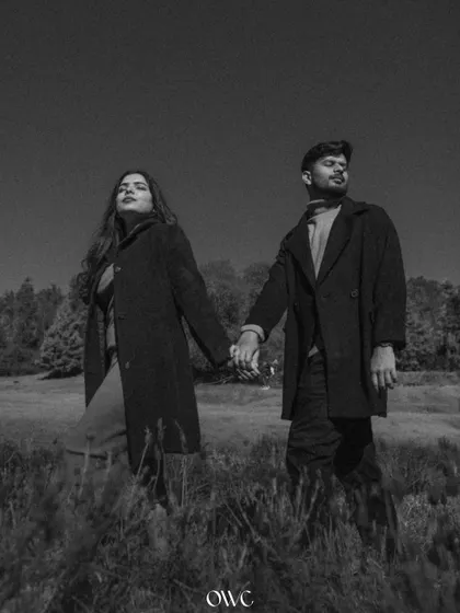 A dramatic black and white portrait of a couple holding hands in a field, giving their pre-wedding shoot a moody and high-fashion feel.