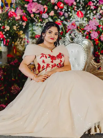 A princess moment. This client is seated on an ornate chair, her voluminous off white ball gown spreading around her. The red floral embroidery on the bodice adds a beautiful pop of color and romance.