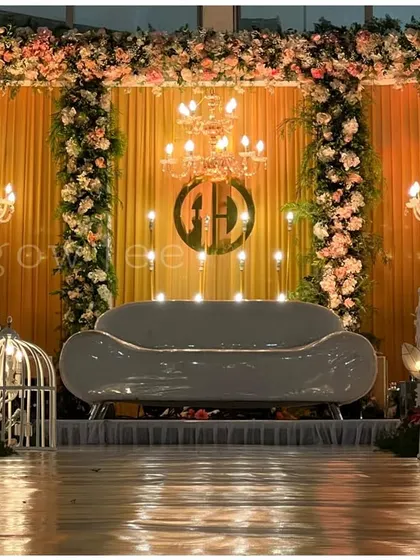 A grand and glamorous reception stage with a golden backdrop, floral arches, and multiple chandeliers.
