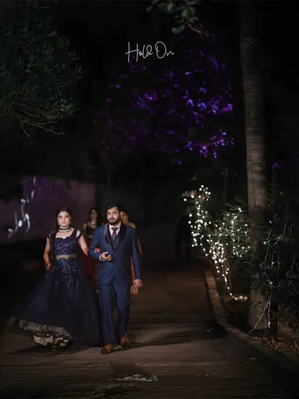 The couple makes their entrance at their evening reception, walking down a path lit by fairy lights, a moment of quiet elegance.