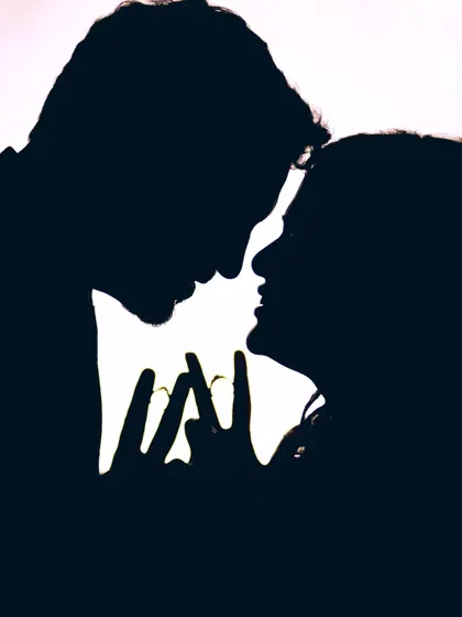 A simple yet powerful silhouette of a couple, their faces close, with their hands forming a heart shape.