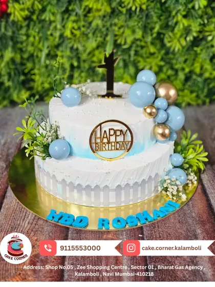 A beautiful two-tier cake in blue and white, decorated with baby's breath and a golden "Happy Birthday" topper. A fresh and elegant design for Roshan's birthday.