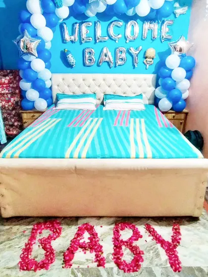 A simple yet sweet 'Welcome Baby' setup for a baby boy, with a balloon arch over the bed and the word 'BABY' written in rose petals.