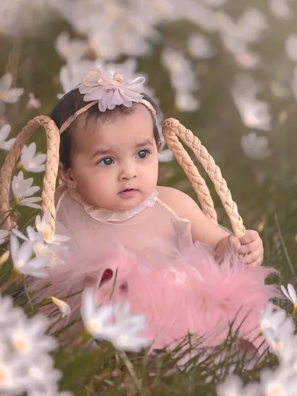 A baby girl sitting in a field of white flowers, looking like a little pixie. This outdoor sitter session uses the beauty of nature to create a magical portrait.