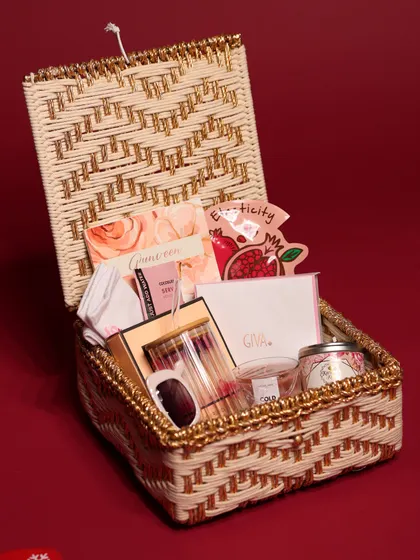 A luxury Christmas hamper for her, packed in a beautiful wicker and gold-threaded basket. It's filled with pampering items, a custom glass, a candle, and jewelry.