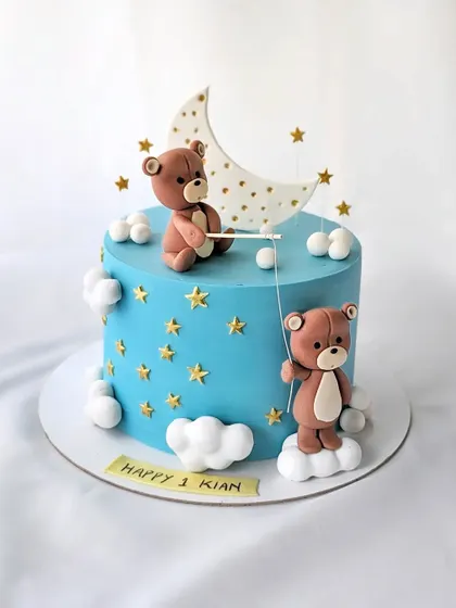 A cute teddy bear cake for Kian's first month birthday. The design features two bears fishing for stars from the moon, set against a dreamy blue sky.