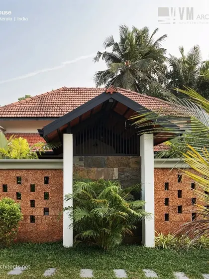 A closer look at the laterite jali wall and traditional gateway at Kuttiyil House, framed by palm trees, perfectly capturing the essence of modern Kerala architecture.