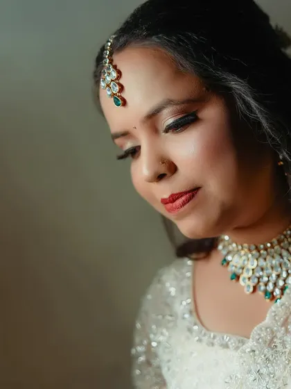 A serene close-up of the bride with her eyes gently closed. The soft lighting beautifully illuminates her makeup, maang tikka, and elegant necklace.
