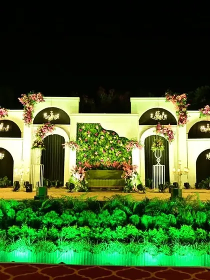 This elegant reception stage shows how I blend classic and modern elements. The clean white arched structure is accented with beautiful chandeliers and soft pink floral arrangements, with a green floral wall as the centerpiece, creating a sophisticated and timeless backdrop.