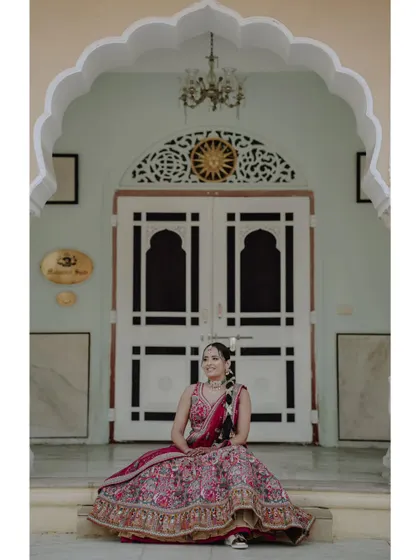 A solo portrait of the bride sitting on the steps of a palace, her vibrant pink lehenga a beautiful centerpiece against the heritage architecture.