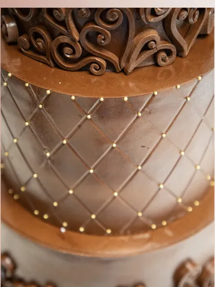 A close-up of the quilted pattern on our luxury chocolate wedding cake. The design is accented with tiny gold pearls, adding a touch of elegance and sophistication to the rich chocolate finish.