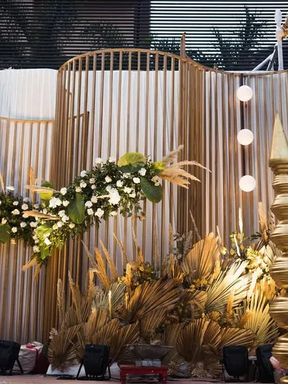 The full view of the bespoke boho mandap, featuring a curved slatted backdrop and dramatic golden accents.