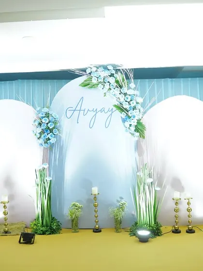 A serene and elegant baby shower backdrop for baby Avyay. The setup uses soft blue and white tones, with arched panels, delicate florals, and rustic accents.