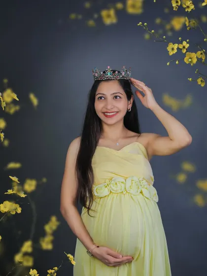 Every mother is a queen. This beautiful studio portrait captures a smiling mom-to-be in a soft yellow dress, adjusting her crown with a gentle touch.