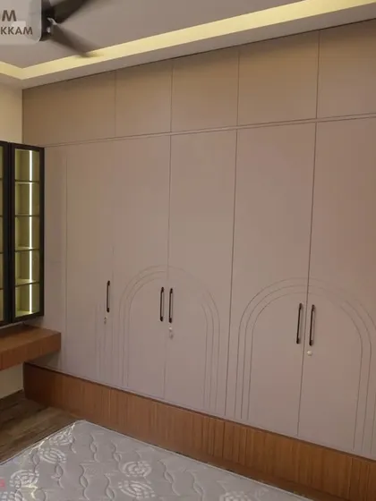 Master bedroom in the Ayyapakkam villa, featuring a large wardrobe with arch-patterned grooves, a built-in dressing table, and an illuminated glass display cabinet.