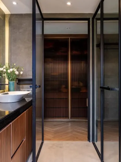 This view showcases the smart layout with a clear division of wet and dry zones. The dual vanity with vessel sinks is separated from the shower and dressing area by sleek, black-framed glass doors.
